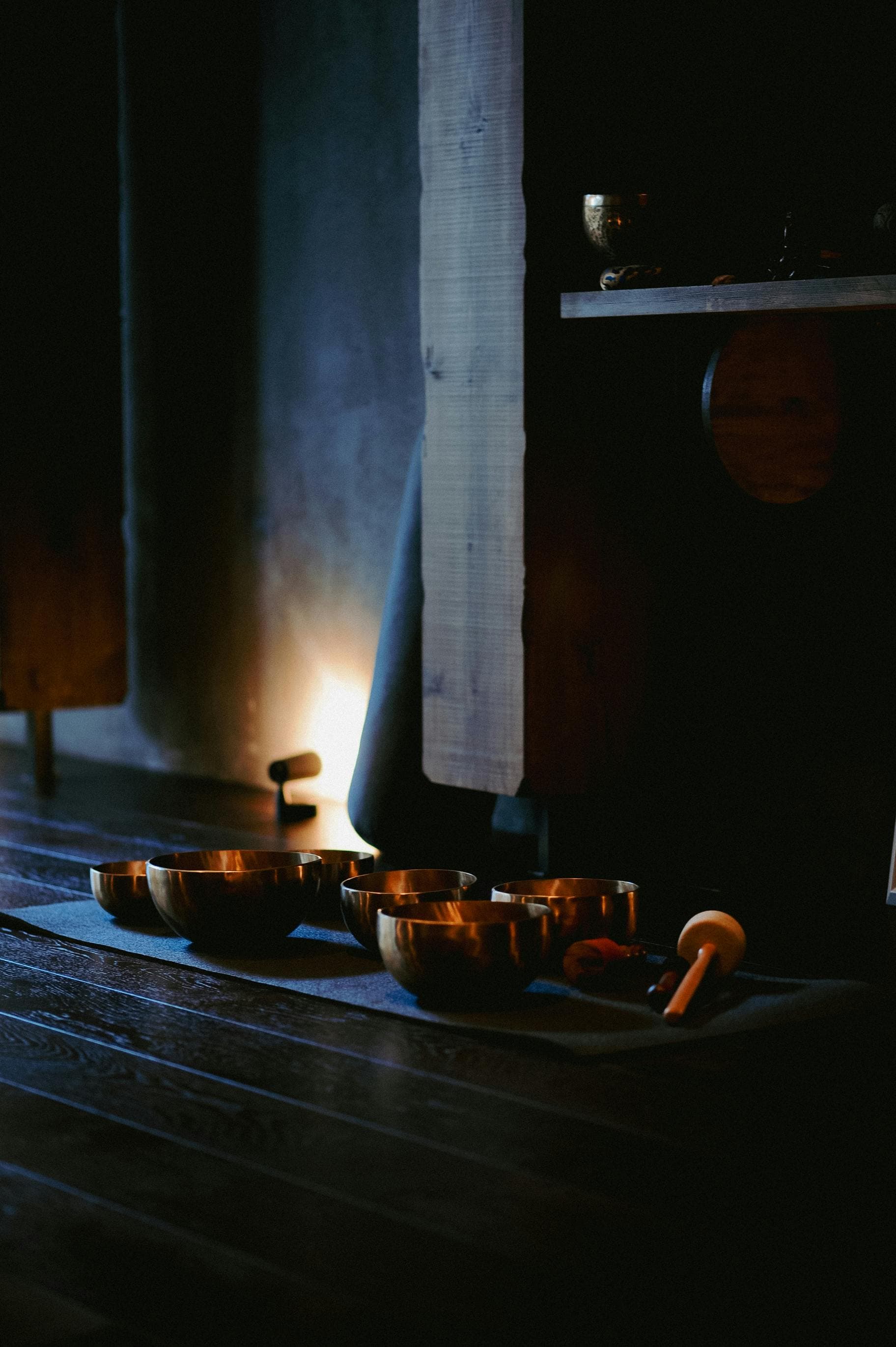 Singing bowls arranged on a dark studio floor near soft candlelight.